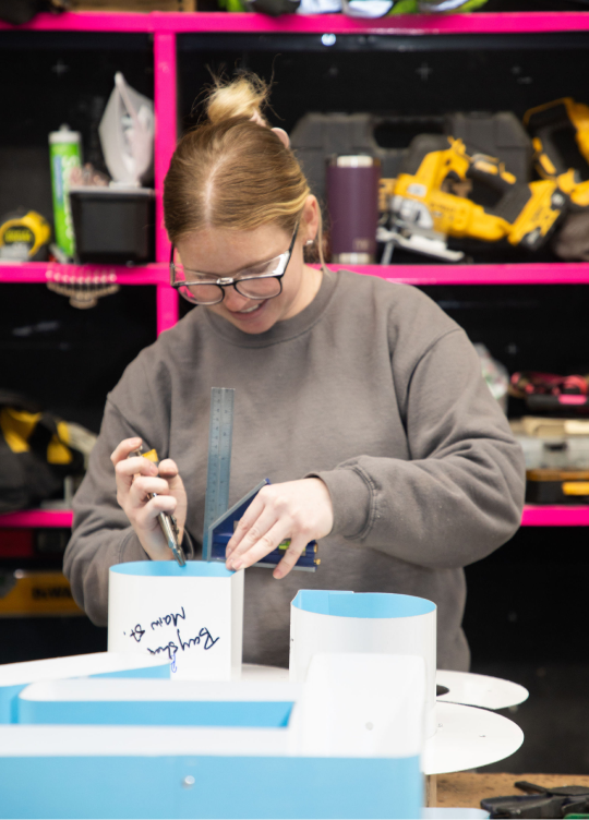 Smiling woman working on a fabrication project in a workshop, using tools for precision assembly.